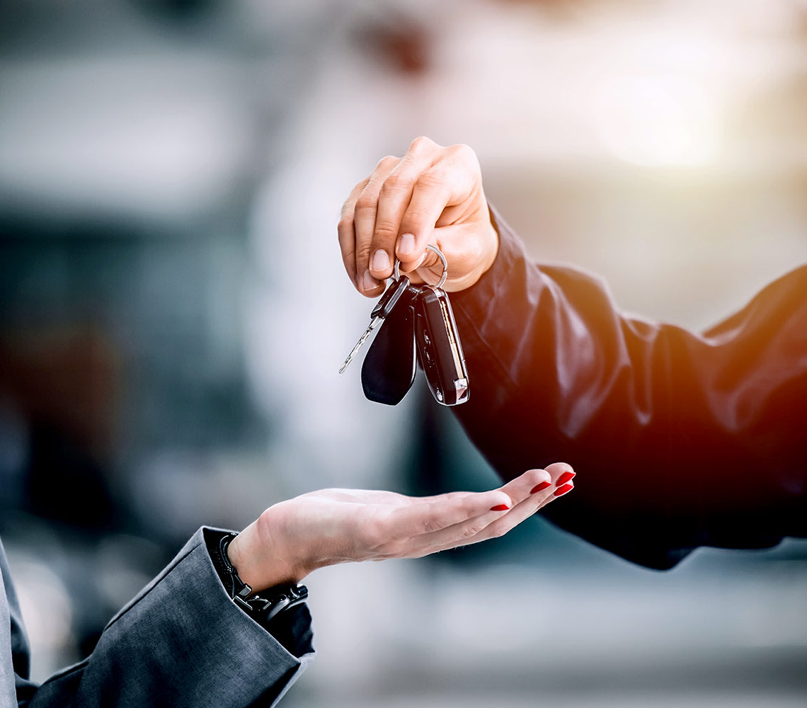 A person is handing a car key to another person, symbolizing a transfer of ownership or responsibility.